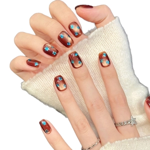 Short square brown cat-eye press-on nails with blue sequin flower accents and warm sweater