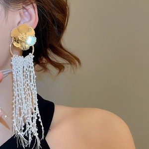 Close-up of long white beaded tassel earrings with gold flower stud on female model