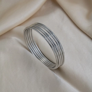 Detail shot of multiple silver stainless steel bangles set on luxury champagne silk fabric