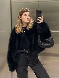 Close-up of black faux fur jacket styled with a woven handbag and metal buckle belt