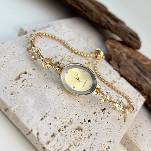 Close-up of gold oval leaf bracelet watch with crystals on a textured stone surface