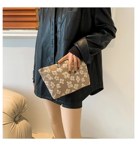 Detail of khaki fabric clutch bag featuring white 3D floral accents held by model
