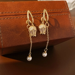 Détail de boucles d'oreilles tulipes dorées avec cristaux et perle blanche sur cuir