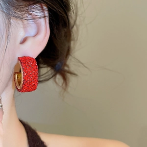 Close-up of elegant gold C-shaped hoop earrings with sparkling red rhinestones on a model