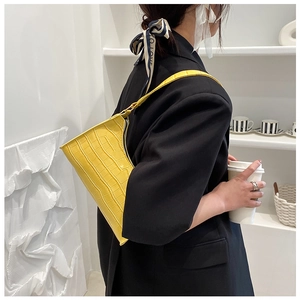 Side view of a bright yellow crocodile pattern underarm bag on a model in a black suit
