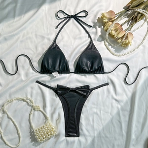 Flat lay of shiny black halter bikini set with decorative bows on white silk background