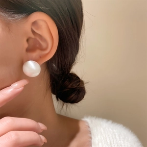 Close-up of a large white round pearl stud earring worn on a model's ear