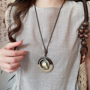 Detail of ethnic style long necklace with wood ring, woven rope, and bronze bird pendant