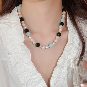 Close-up of beaded necklace with light blue and pearl beads on a ruffled white shirt