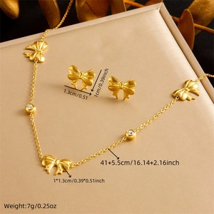 Gold plated bow necklace and earrings set with zircons on a beige jewelry box