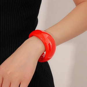 Detailed view of wide irregular wave red resin bangle worn on model with black knitwear