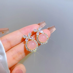 Detailed close-up of bow knot earrings with pink cat eye stone and zircon in gold finish
