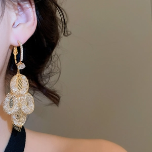 Detailed close-up of golden leaf tassel earrings with sparkling zircons on model ear