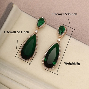 Detail view of emerald teardrop earrings with gold pave setting in a jewelry box