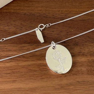 Macro shot of 925 sterling silver rose pendant and clasp on a rustic wooden background
