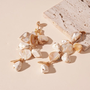Detail of bohemian gold drop earrings featuring shell slices and irregular faux stone beads