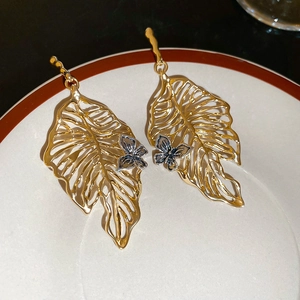 Detail of gold hollow leaf earrings with small silver butterfly accents on ceramic plate