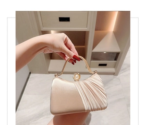 Detail of champagne satin evening bag with pearl clasp and metal handle held by hand