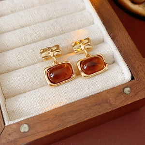 Vue macro des boucles d'oreilles carrées en résine ambre plaqué or dans une boîte en bois