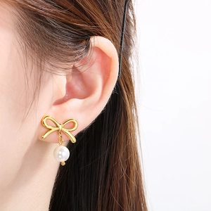 Detail of elegant gold bow earrings with a single white pearl drop on a female model