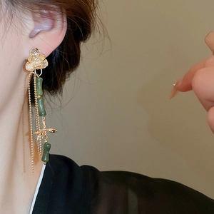 Close-up of long tassel earrings with green beads and gold bamboo nodes on a model