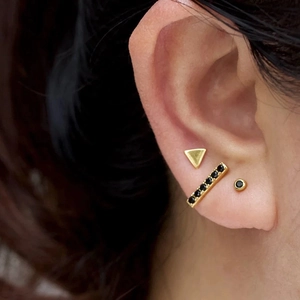 Close-up of three geometric gold stud earrings with black zircon on earlobe
