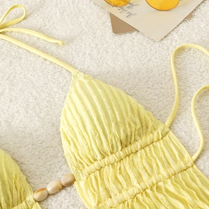Detail of light yellow textured bikini top featuring beaded drawstring and seashell accents