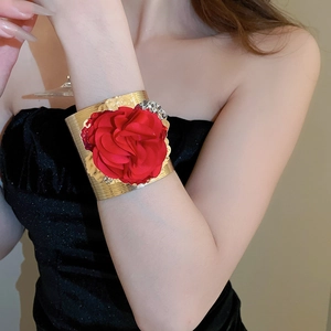 Detail of wide gold cuff bracelet featuring a large 3D red fabric flower on model wrist