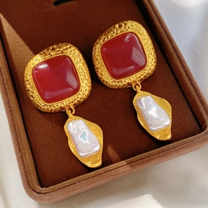 Detail of vintage gold-hammered earrings with red resin stones and baroque pearls
