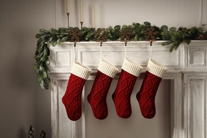 Macro detail of red knitted Christmas stockings with cable pattern hanging on a white fireplace