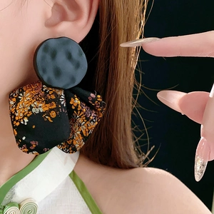 Detail of round textured metal stud with orange and gold floral silk drop on ear