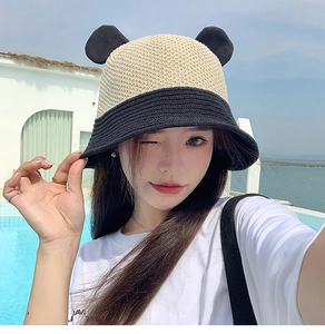 Detailed view of bicolor straw bucket hat with bear ears worn by model outdoors