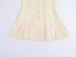 Détail d'une robe en tweed beige avec boutons décoratifs et ourlet de jupe plissé