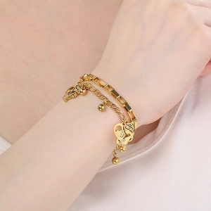 Detail of layered gold stainless steel bracelet with heart pendant on woman's wrist