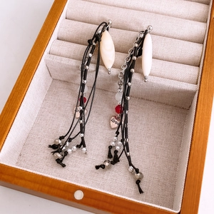 Detail showing handwoven tassel earrings with shell beads and silver heart pendants