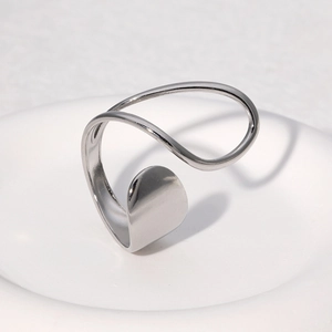 Bague ouverte argentée minimaliste au design abstrait posée sur plateau céramique