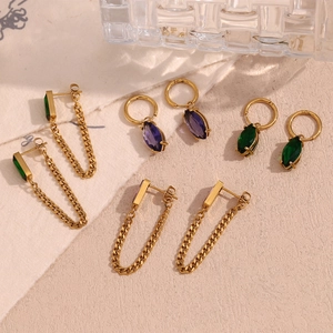 Macro shot of 18K gold plated earrings with purple and green zircon crystals on white surface
