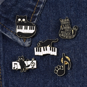 Set of five black cat enamel pins with musical notes on blue denim background