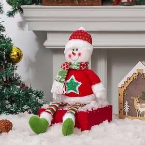 Poupée bonhomme de neige de Noël avec bonnet rayé assise près de la cheminée décorée