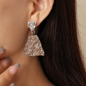 Detail of asymmetric geometric hammered metal earrings on model showing textures
