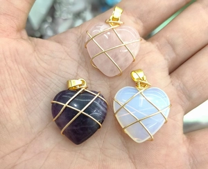 Detail of three handmade wire-wrapped heart crystal pendants in pink, purple, and opal