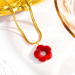Detail of red flower pendant on golden snake chain over white marble background