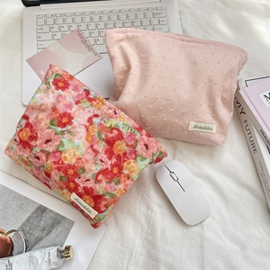 Flat lay of floral and pink dot makeup bags with a laptop and accessories on white cloth