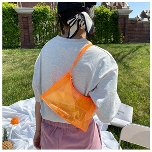 Detail shot of a transparent orange PVC baguette bag in a sunny outdoor picnic setting