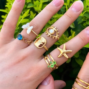 Detail of stacked gold stainless steel rings with butterfly, star, and natural stone