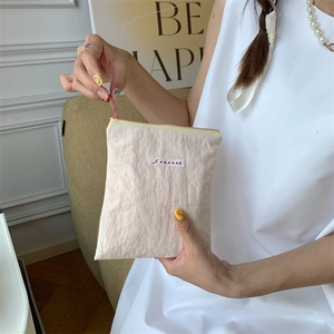 Close-up of a cream-colored textured mini makeup bag with zipper and logo held by a hand