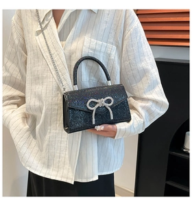 Détail d'un sac à main noir pailleté avec une boucle nœud en strass et une bandoulière chaîne