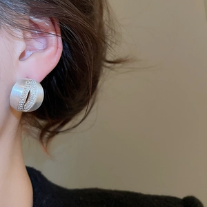 Macro detail of brushed silver C-shaped earrings with zircon inlay on a model