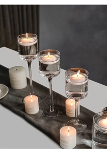 Dettaglio di eleganti portacandele in vetro a stelo con candele galleggianti per nozze
