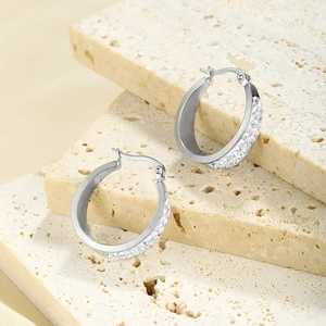 Close-up of silver stainless steel hoop earrings with double-row crystals on stone surface